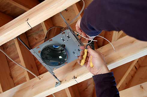 Electrician connecting can lighting to wooden floor joists